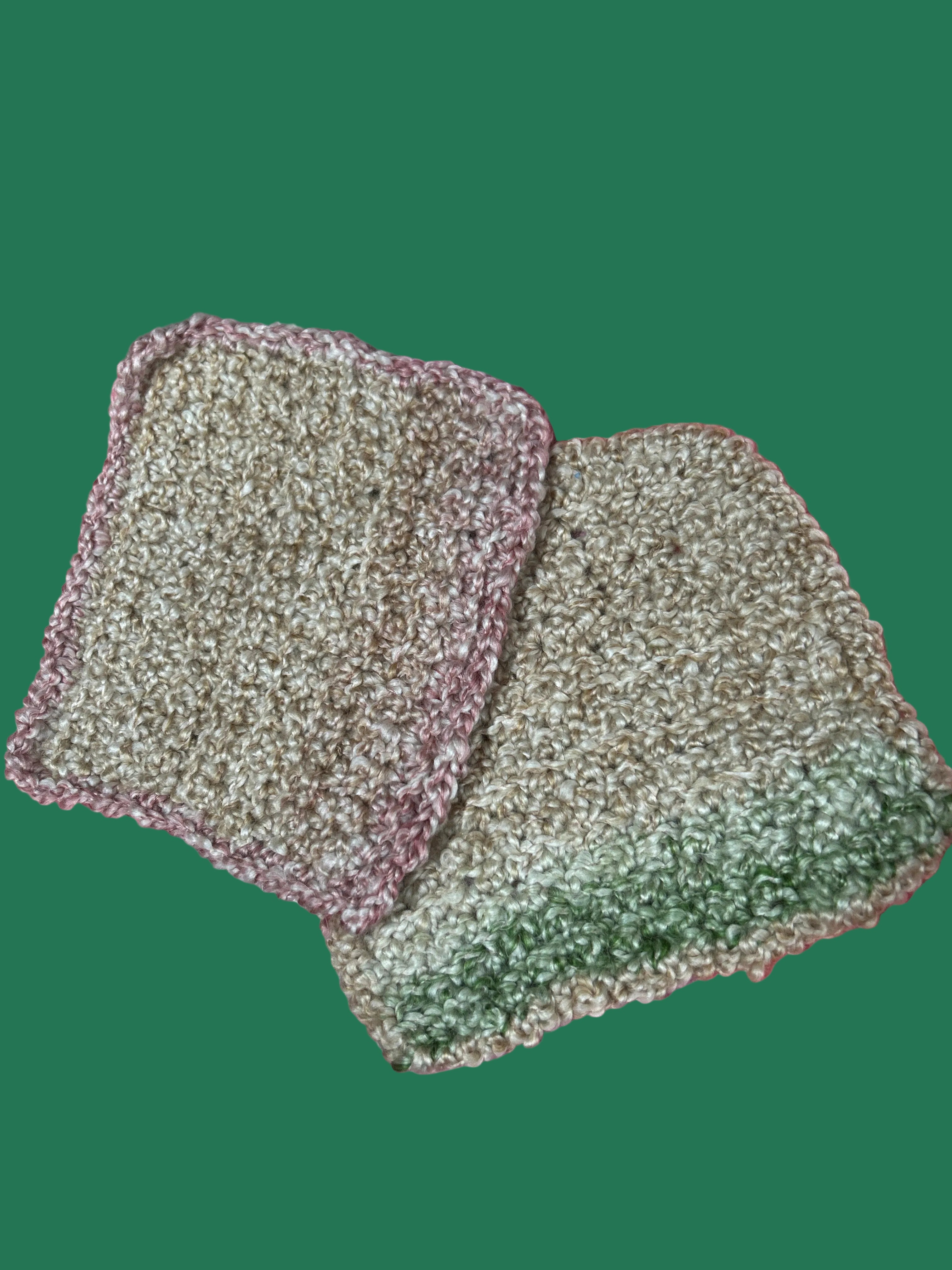 Two green scrubbing pads on a pink surface with plastic wrap.