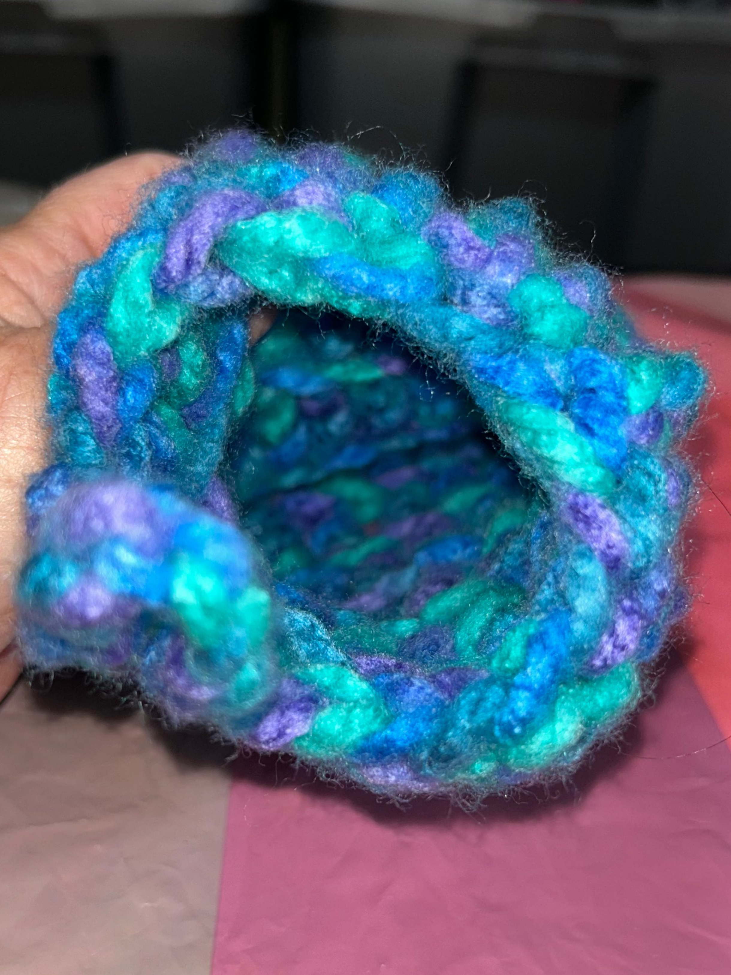 Hand holding a colorful knitted item on a pink surface with a blurred background