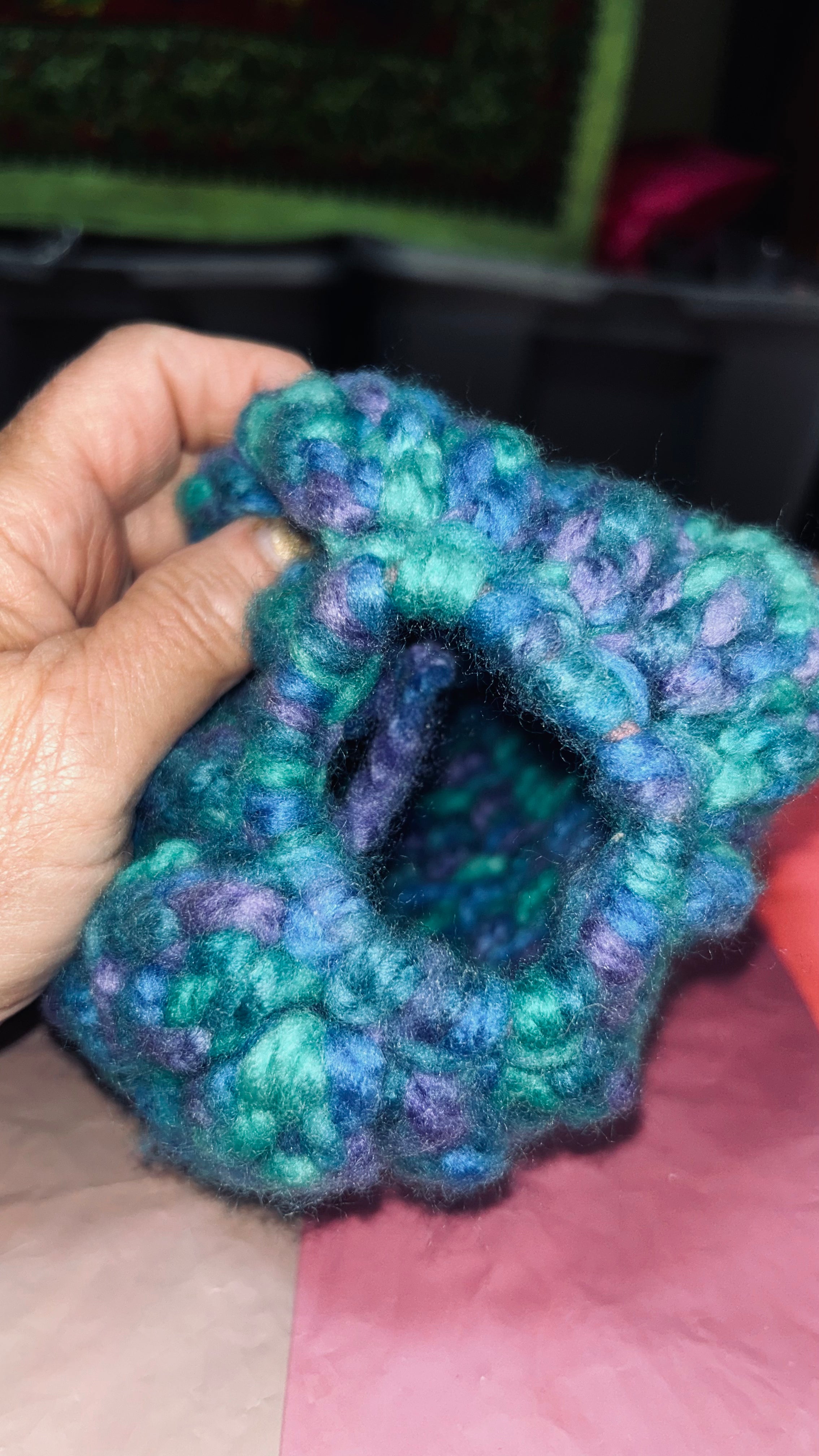 Hand holding a knitted green and purple scrunchie.
